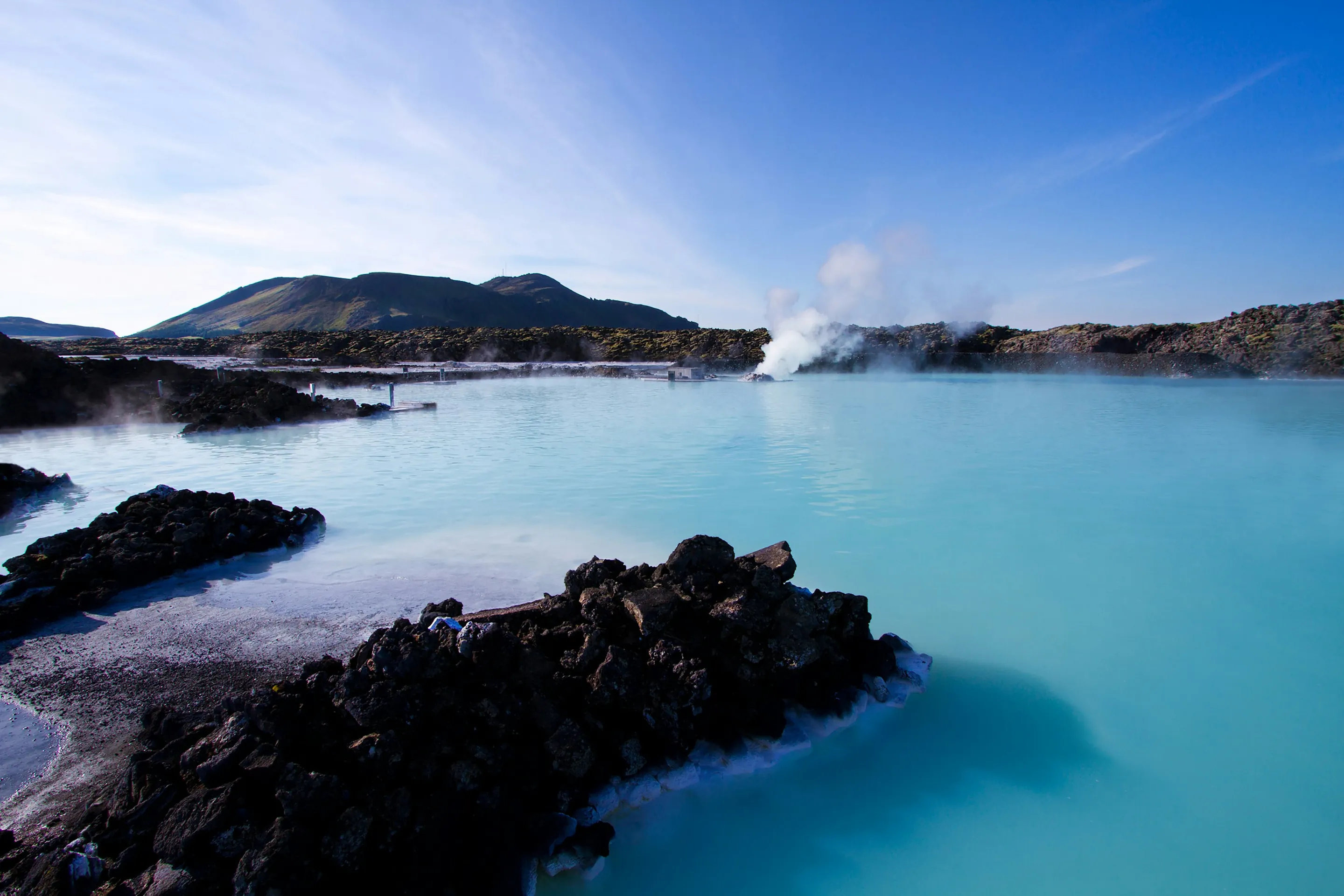 Milky-blue water of the Blue Lagoon between black lava rocks, steam rising