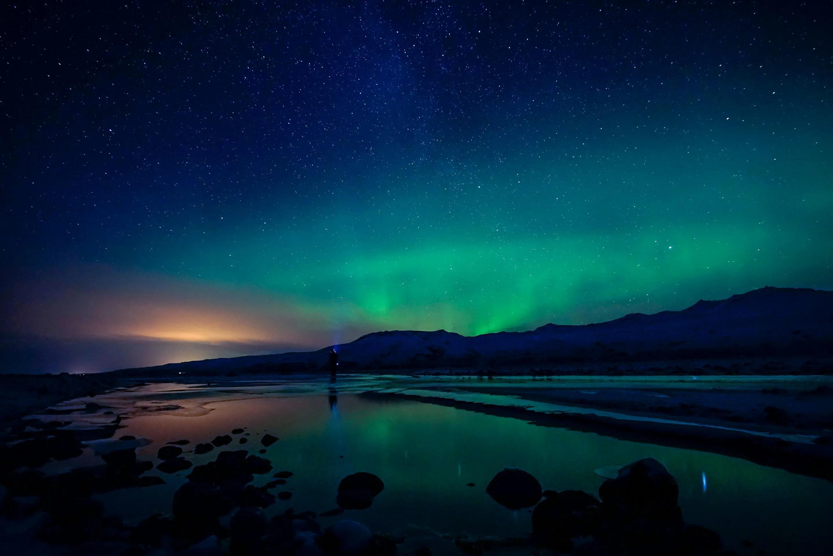 Green northern lights over a still lake and dark mountains at night