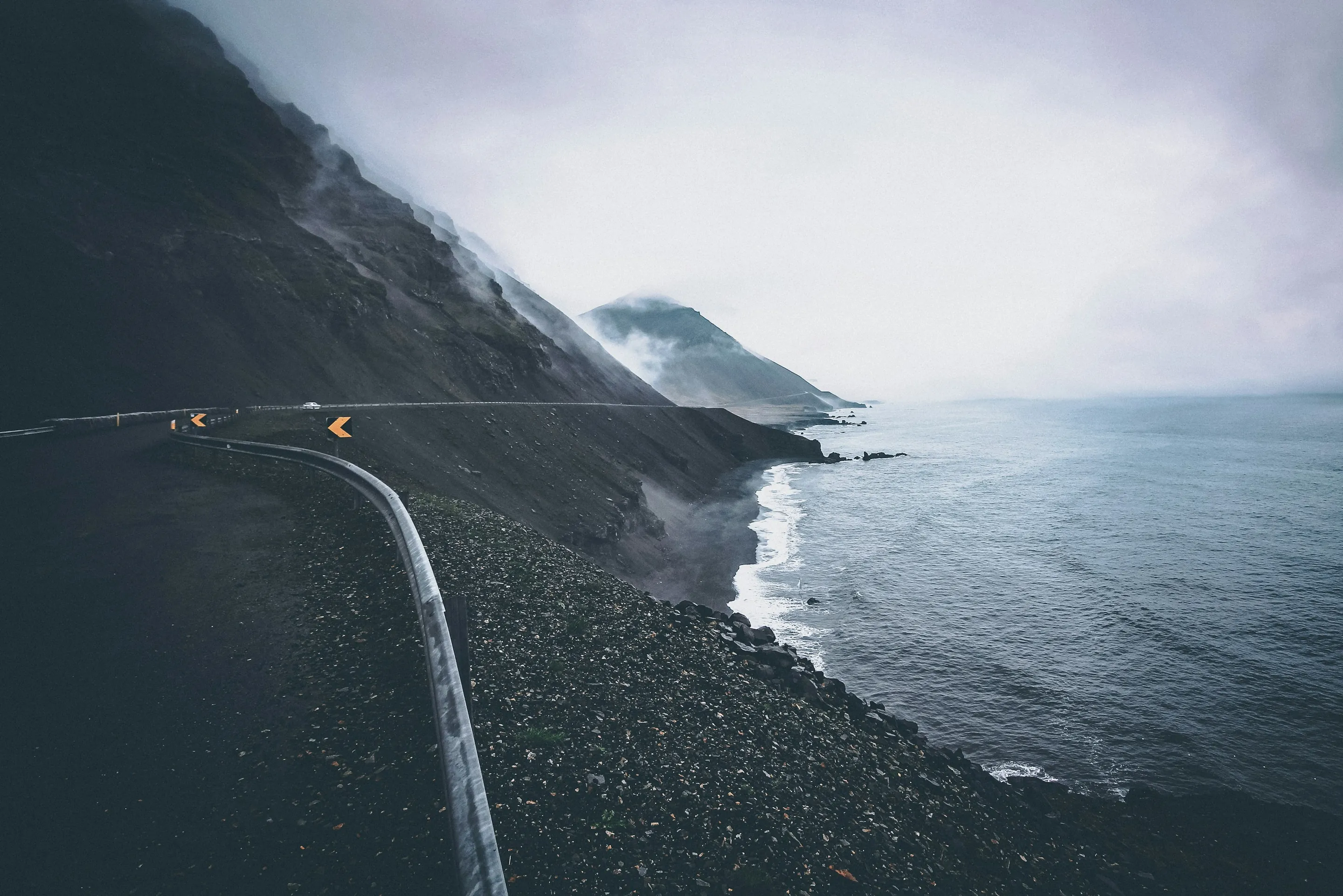 A coastal road curving along a dark shore under low cloud